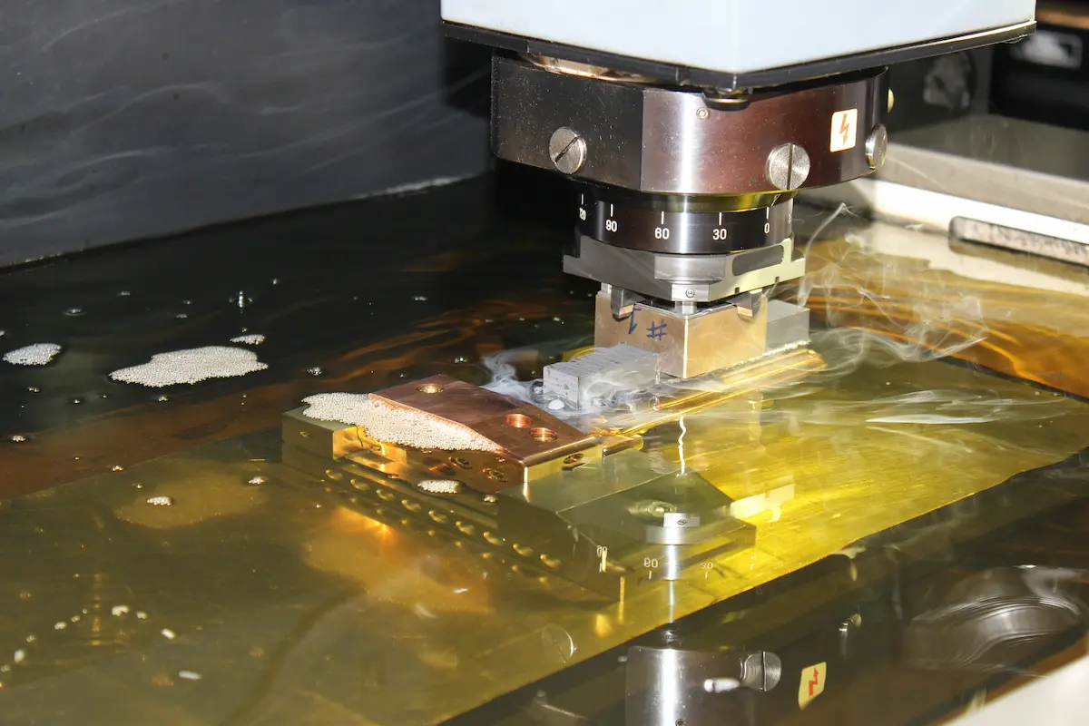 Wire EDM machine cutting a brass workpiece submerged in dielectric fluid